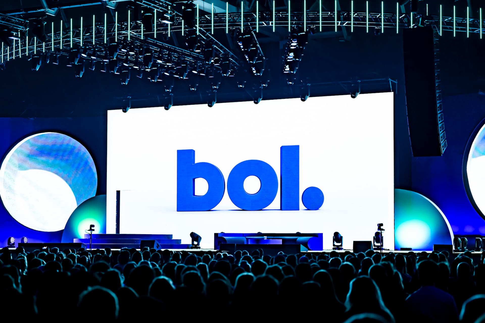 a group of people in an audience looking at the stage which has the bol logo behind it