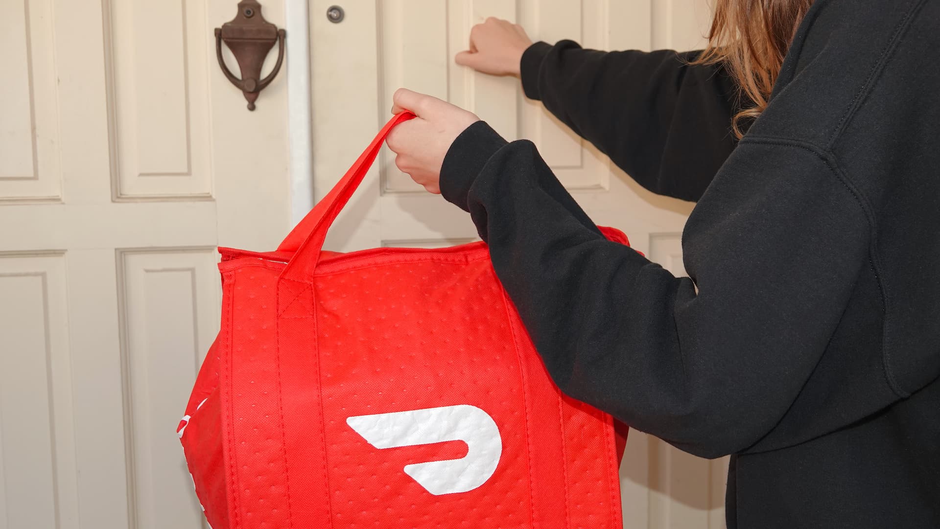 A lady holding a bag of shopping knocking on a front door