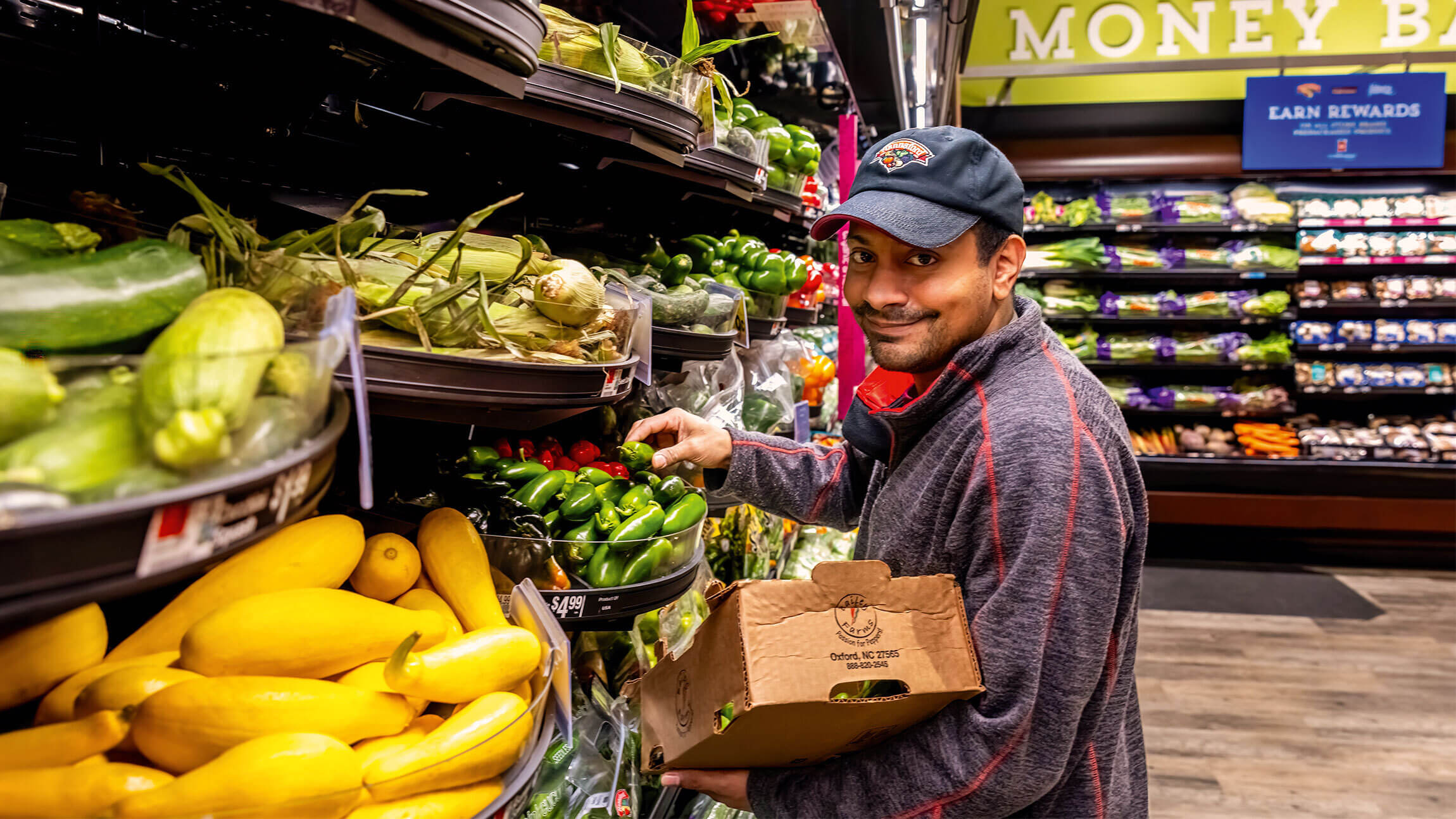 A man smiling at the camera packing some bananas into a box