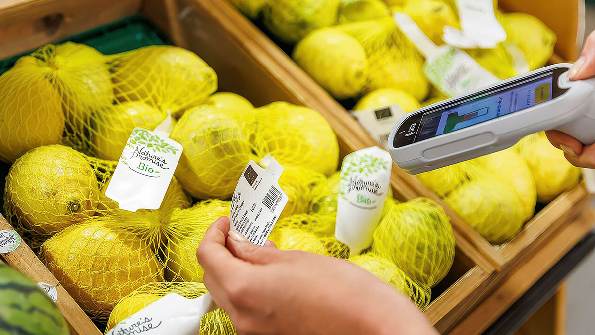Person scanning barcode on netted yellow organic lemons labeled Nature's Promise Bio in wooden crates at a market.